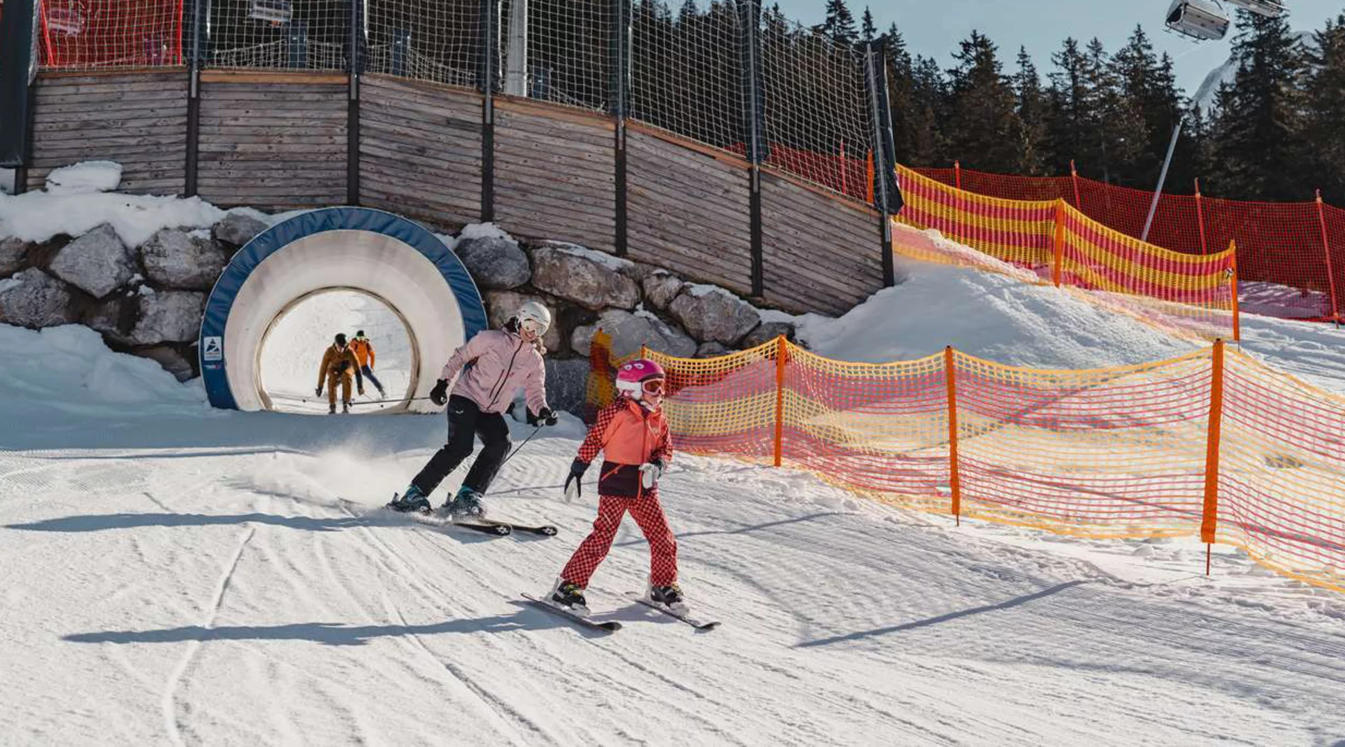 Skifahren Ehrwalder Alm | © Tiroler Zugspitz Arena/Sam Oetiker Eine Familie fährt mit Skiern durch einen Tunnel in der Funslope im Skigebiet Ehrwalder Alm | © Tiroler Zugspitz Arena/Sam Oetiker