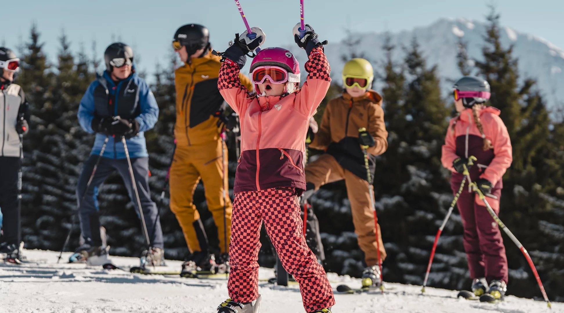 Skiing with the family | © Tiroler Zugspitz Arena/Oetiker Sam A child on skis is happy and raises his poles in the air, with the family behind him | © Tiroler Zugspitz Arena/Oetiker Sam