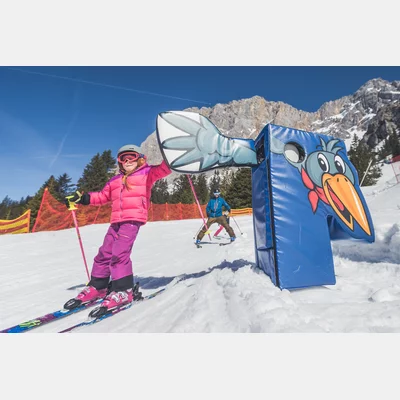 Ein skifahrendes Kind klatscht mit einer großen Hand ab, welche neben der Skipiste aufgestellt ist | © TZA/ C.Jorda