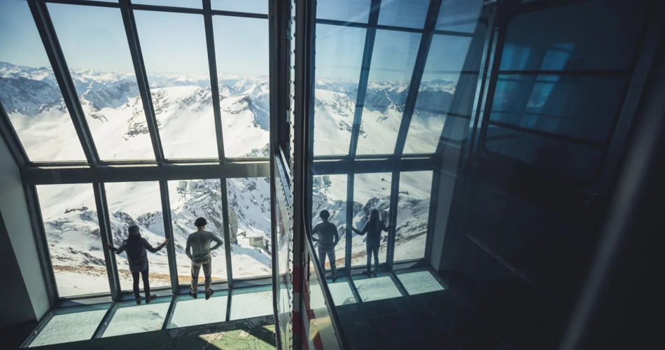 Ein Paar schaut durch das Fenster von dem Museum Faszination Zugspitze Richtng Zugspitzplatt | © Tiroler Zugspitz Arena/ Christoph Jorda