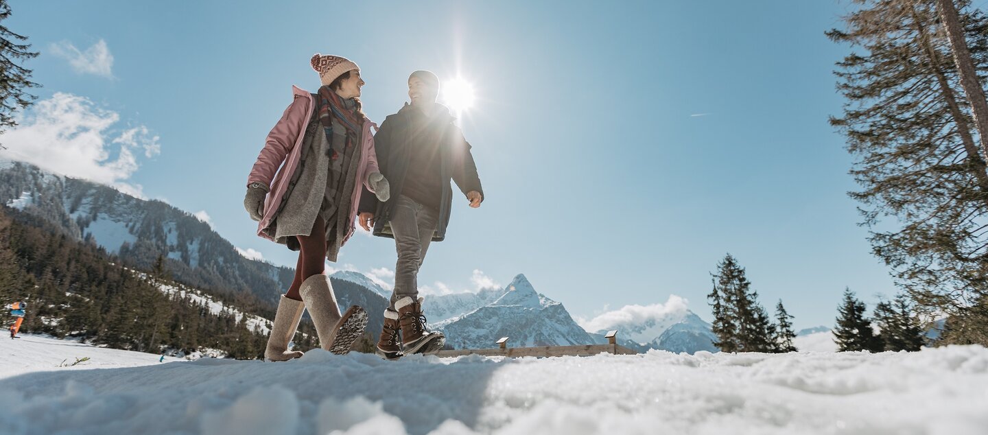 Schneebedeckter Hügel auf dem ein Mann und eine Frau spazieren gehen, im Hintergrund die leicht wolkenumhangene, verschneite Zugspitze. | © (c)ZABT_C. Jorda (66)